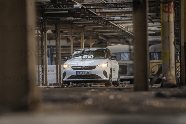 A white Opel with car sharing logo stands between other vehicles in an old industrial building,