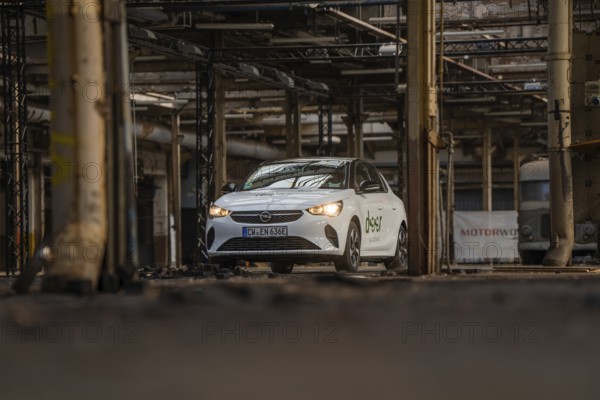 A white car with car sharing logo is parked in an old industrial building, Deer E-Car Sharing,