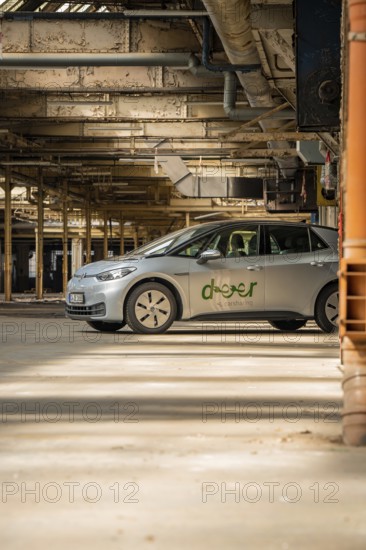 A car with the car sharing logo is parked in a light-flooded industrial building, Deer E-Car