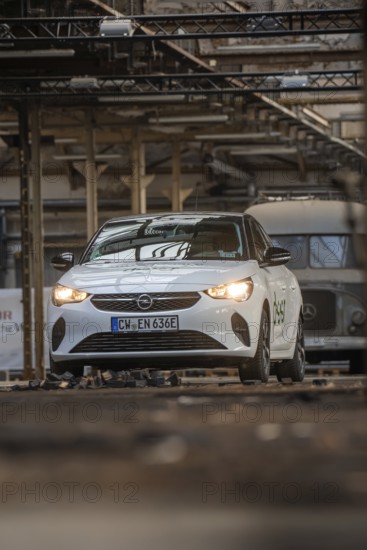 White Opel with car sharing logo in an urban industrial building with visible metal structures,