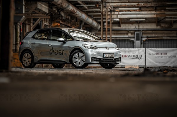 An electric vehicle is parked in an empty, urban factory building with visible pipes and