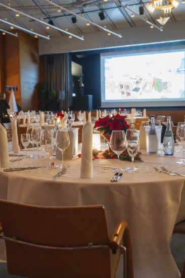 An elegant banquet hall with festively decorated tables and a projection screen in the background,