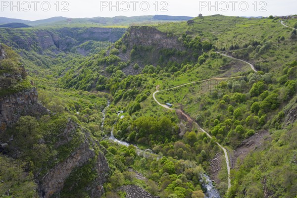 Lush green gorge with winding paths along which a river flows, surrounded by mountains, Dashbashi