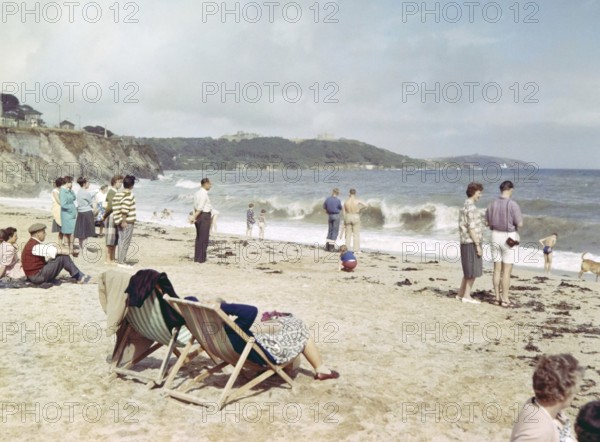 People on sandy beach looking at breaking waves, Gyllyngase beach, Falmouth, Cornwall, England, UK