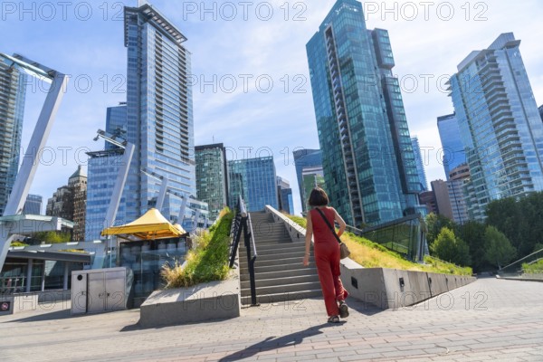 Tourist walking up stairs in downtown vancouver with modern skyscrapers, green roof and blue sky in