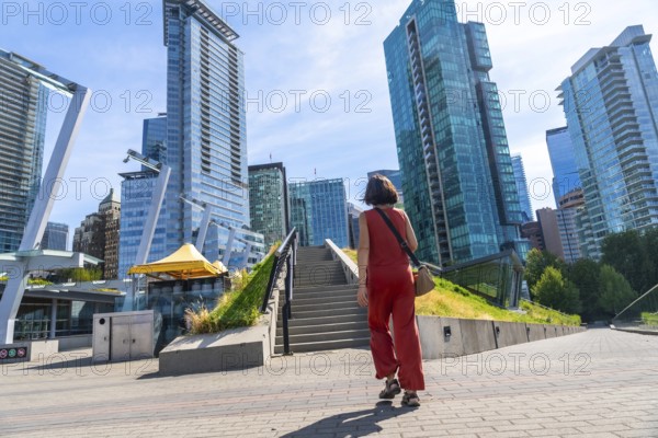 Young woman tourist walking up stairs in a modern city park with skyscrapers and office buildings