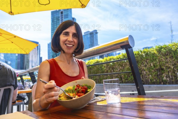 Happy woman enjoying a healthy poke bowl at an outdoor restaurant patio in vancouver, british