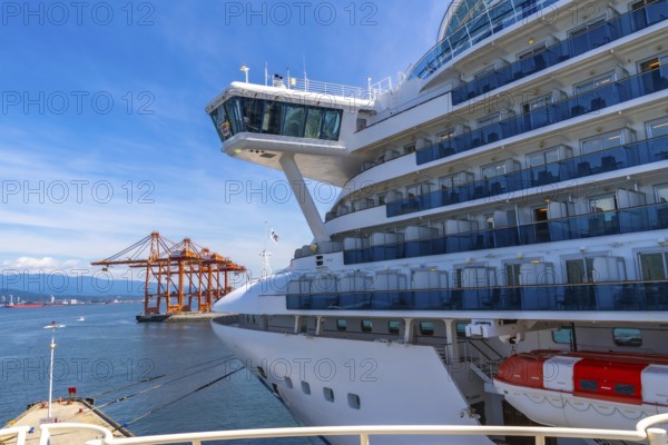 Large white cruise ship docking in vancouver harbor, surrounded by towering cargo cranes and