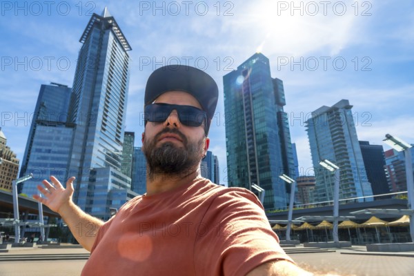 Happy bearded tourist wearing sunglasses and a baseball cap is taking a selfie with outstretched