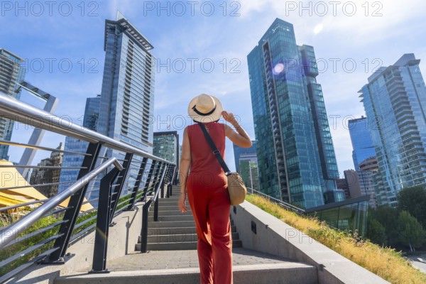 Female tourist wearing a straw hat and holding her hat is walking up stairs with modern glass