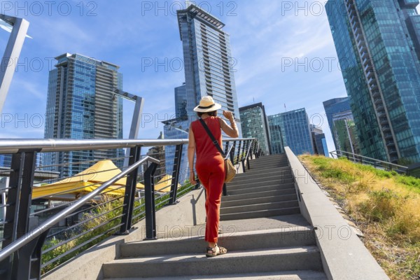 Female tourist wearing a straw hat and red jumpsuit walking up stairs in downtown vancouver,