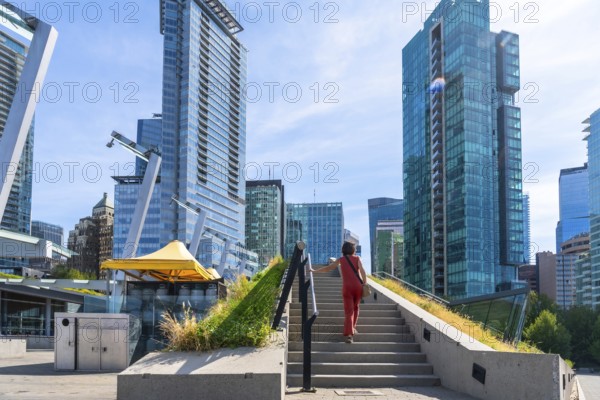 Businesswoman climbing stairs in a green urban space with skyscrapers in the background in