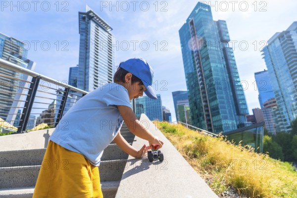 Young boy playing joyfully with a toy car on the steps of an urban park, soaking up the warmth of a