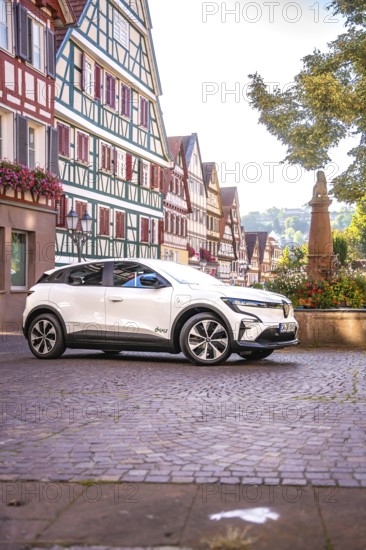 White car in an old town with magnificent half-timbered buildings and a statue, Deer E-Carsharing,