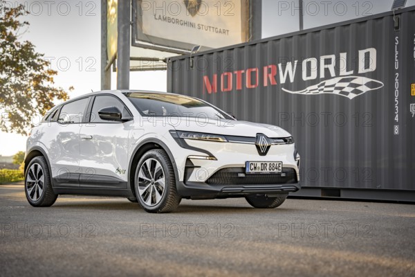 A white electric car stands in front of a Motorworld container on a concrete surface, Deer