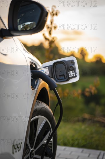 A white electric car is charged by a charging cable at sunset, Deer E-Carsharing, Renault Megane,
