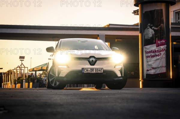 Car with bright headlights in an urban environment at night in front of posters, Deer E-Carsharing,