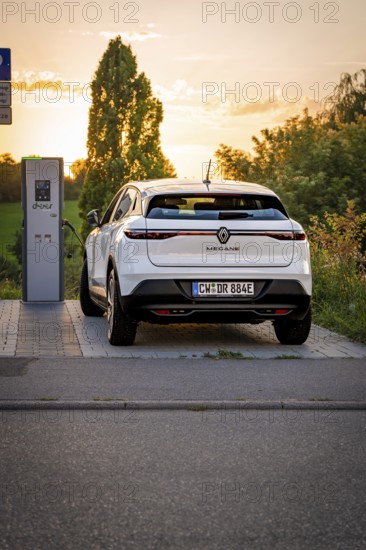 An electric car is connected to a charging station surrounded by the setting sun, Deer