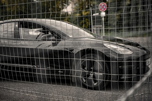 Black car behind a metal grid in an urban environment, Deer e-Carsharing, Tesla Model 3, Calw,
