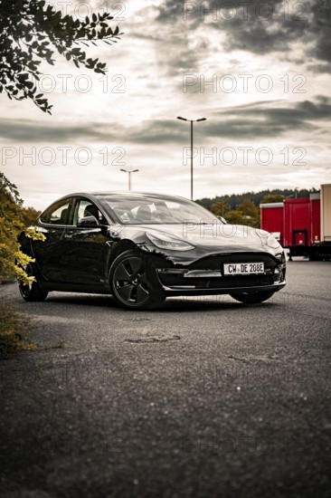 Black car on an empty side of the road surrounded by trees and a cloudy sky, Deer E- car sharing,