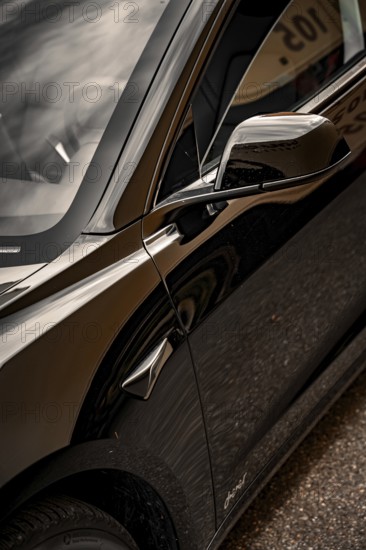Close-up view of the side mirrors and body of a black car with shiny surface, Deer E-Carsharing,