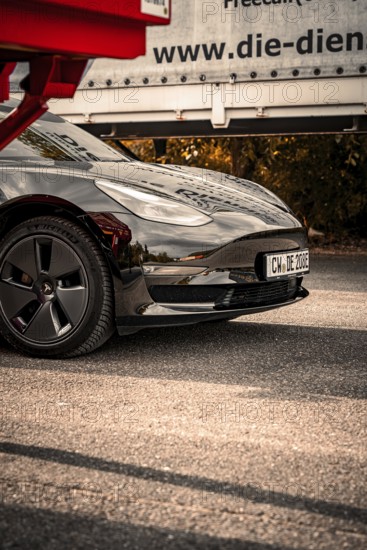 Close-up of a black car with shiny paint and visible reflection on the asphalt, Deer E-Carsharing,