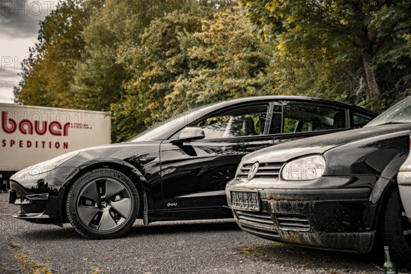 Black car and older vehicle in a parking lot with a truck in the background, Deer E-Carsharing,