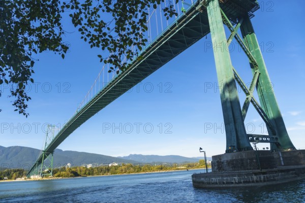 Lions gate bridge extending over burrard inlet with stanley park seawall in foreground and north