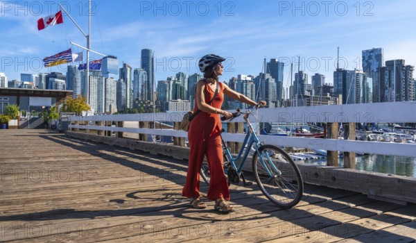 Female tourist wearing a helmet is walking alongside her bicycle on a wooden pier, enjoying the
