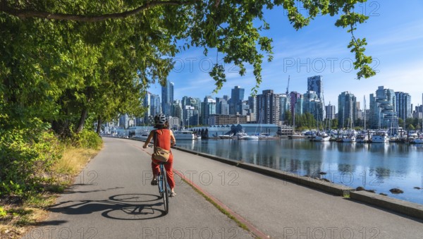 On a sunny summer day, a woman enjoys a leisurely bike ride along the seawall in stanley park, with