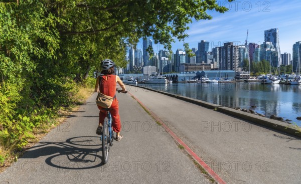 Tourist wearing helmet and orange jumpsuit is riding bicycle on seawall in stanley park with