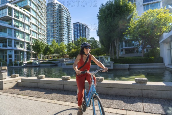 Woman wearing a helmet and sunglasses is riding a bicycle along a waterfront path in vancouver,