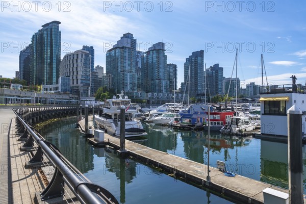Modern buildings rise above a marina filled with yachts and houseboats, creating a picturesque
