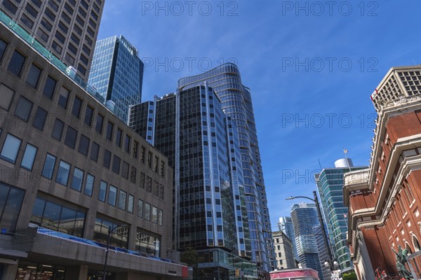 Modern glass skyscrapers and historical brick buildings stand tall against a vibrant blue sky,
