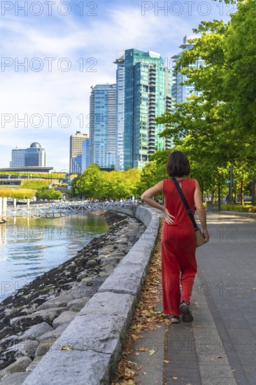 Tourist walking on the seawall in vancouver downtown with modern buildings and green trees in the