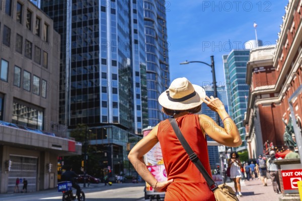 Female tourist wearing a straw hat and an orange dress is admiring the skyline of vancouver,