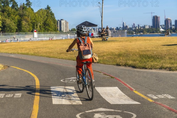 Tourist enjoying cycling in kitsilano beach park with english bay and the city of vancouver skyline