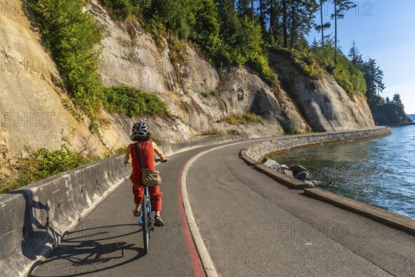 Tourist wearing helmet and carrying bag is riding bicycle along stanley park seawall in vancouver,