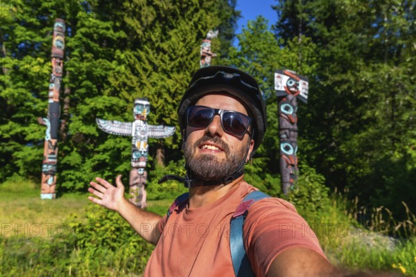 Cyclist wearing a helmet and sunglasses takes a selfie with totem poles at brockton point in