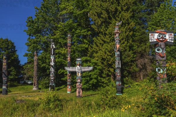 Totem poles standing tall against a backdrop of lush trees and blue sky, showcasing the rich