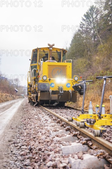 Yellow rail vehicle on tracks in foggy forest landscape, surrounded by tools, stuffing machine on