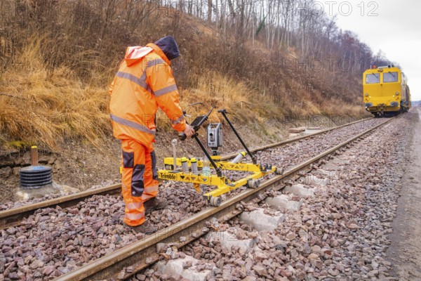 A worker operates a yellow device on the railroad tracks in an autumn landscape, stuffing machine