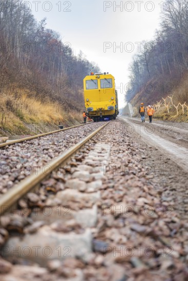 Yellow vehicle crosses rails, workers work on the track in the forest, tamping machine on Hermann,