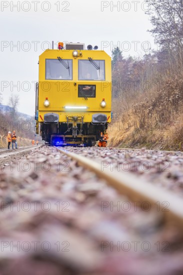 Yellow vehicle on gravel with construction workers in the forest, tamping machine on Hermann,