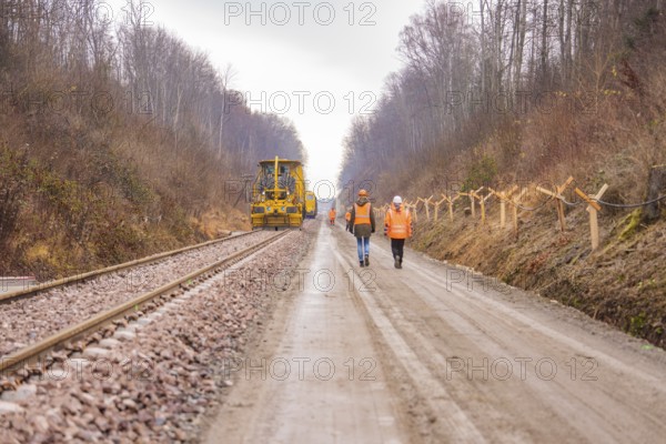Construction worker and machine tool working on a railroad track in the forest, tamping machine on