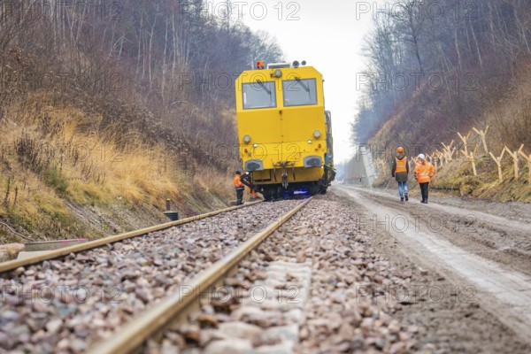 Yellow vehicle on rails with construction workers on a gravel path in the forest, stuffing machine
