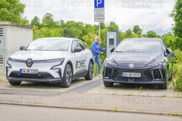 Two electric cars are parked at the outdoor charging station with a woman nearby, Deer E-