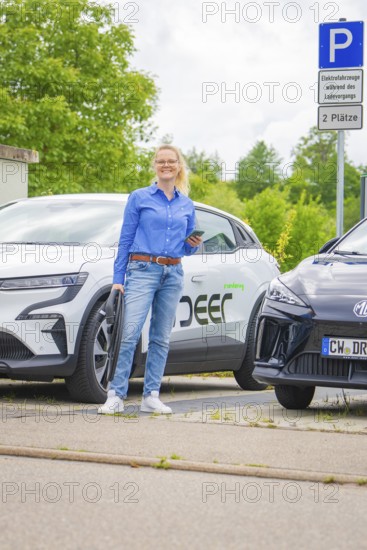 Woman standing in front of two electric cars in a parking lot with technological flair, Deer