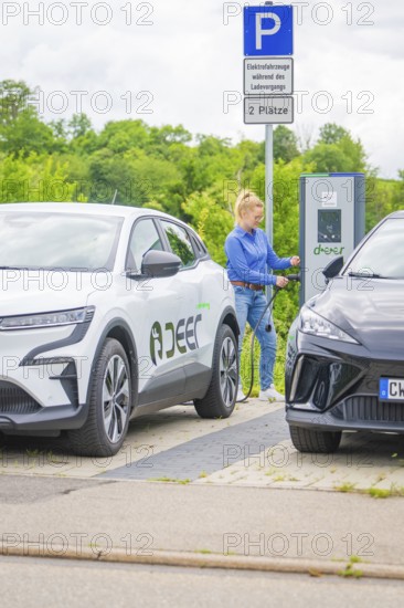 Woman connects Renault electric car to charging station in a municipal parking lot, Deer