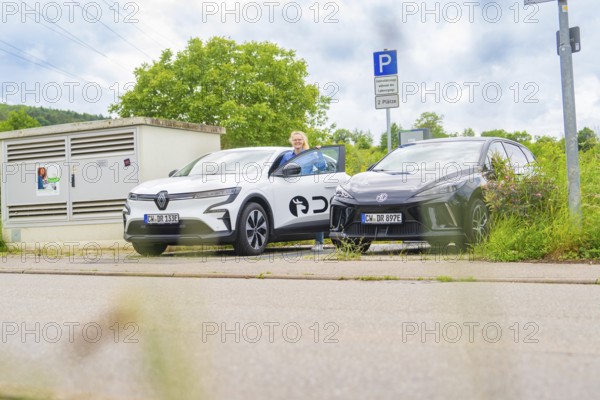 Two electric cars are parked in a parking lot, and a man is standing next to them. Cloudy sky and